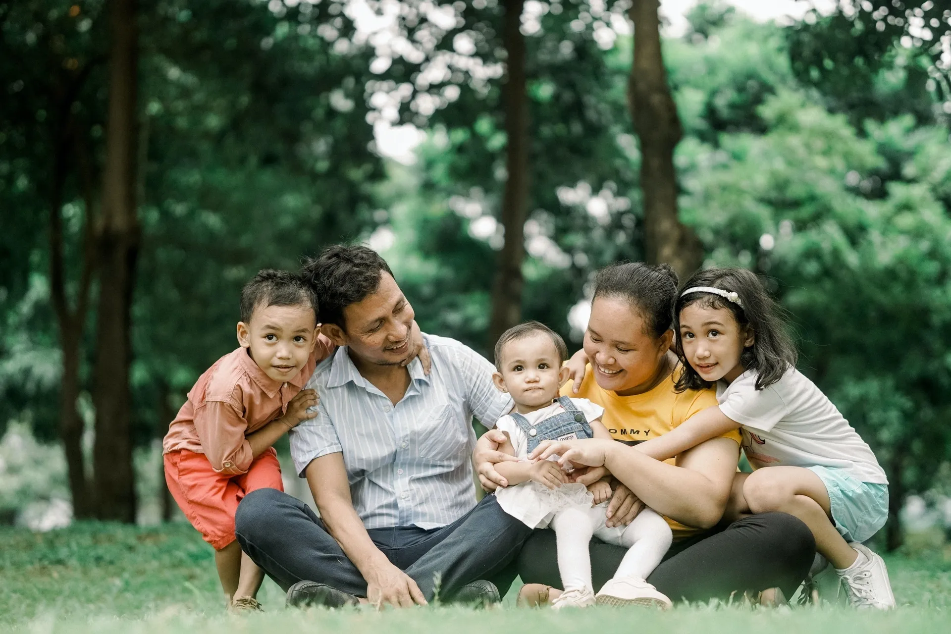A family of four enjoying a sunny day, sitting together on the grass in a park.